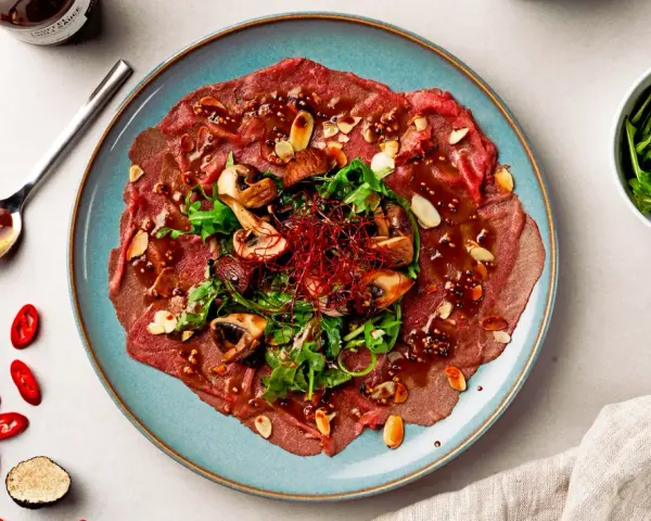 Carpaccio vom Rind mit Pilzen, Rucola und Mandeln, garniert mit Chili und Trüffel. Ein Gericht, das zeigt, was ist Carpaccio.