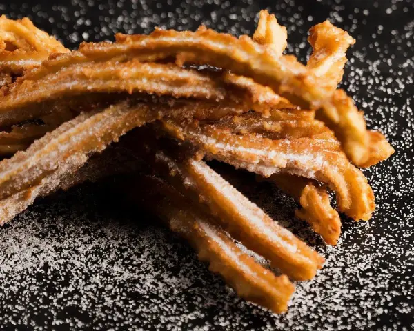 Krispiga churros, pudrade med socker, redo att avnjutas. Ett enkelt churros recept för hemmabruk.