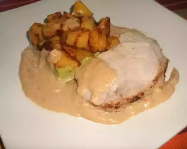 Tranche de roti de porc au lait, nappée d'une sauce onctueuse, accompagnée de pommes de terre rôties croustillantes. Un plat réconfortant.