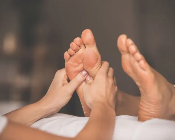 Hands giving a relaxing foot rub to a person lying on a white surface.