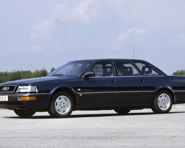 Ciemnoniebieski Audi V8 z lat 90. stoi na pustej drodze, z drzewami w tle.