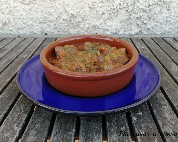 Goulash de ternera humeante en cazuela de barro, servido sobre plato azul. Un plato reconfortante listo para disfrutar.