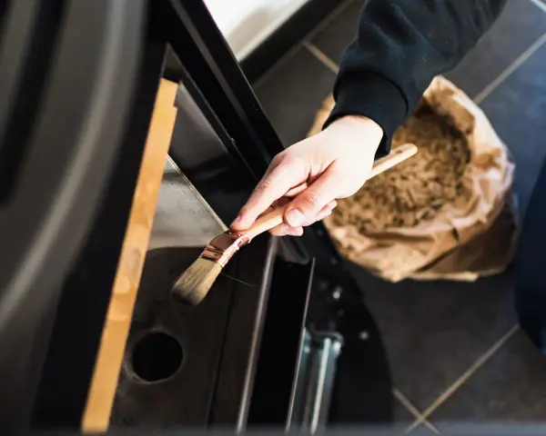 Mano che pulisce la stufa a pellet con un pennello. La manutenzione stufa a pellet ogni quanto è fondamentale per l'efficienza.