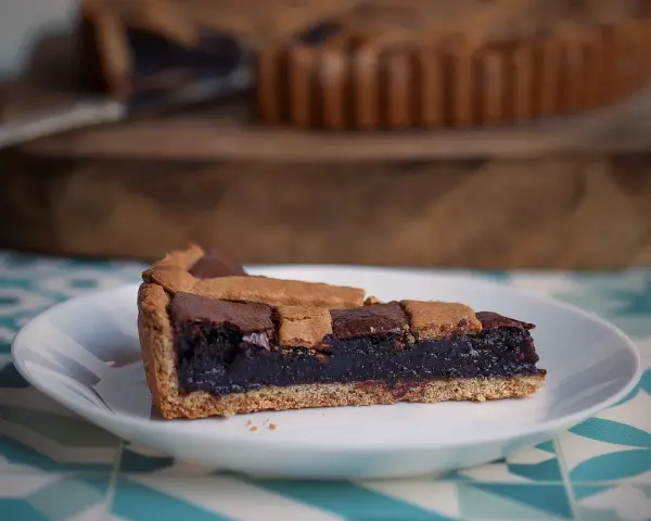 Una fetta di crostata al cioccolato, con la sua base dorata e il ripieno scuro e invitante, pronta per essere gustata.