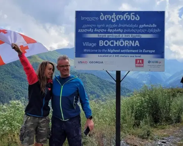 Para, z gruzińską flagą, na tle gór i znaku "Wioska Bochorna", najwyżej położona osada w Europie. Podróżując, warto zapytać: czy w Gruzji jest bezpiecznie?