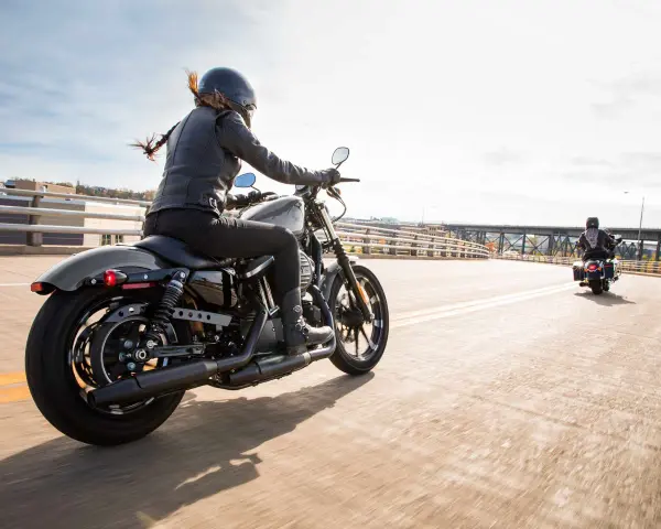 Kobieta w skórzanej kurtce i kasku jedzie na stylowym motocyklu dla kobiety. Wiatr rozwiewa jej włosy, a słońce odbija się od chromowanych elementów.
