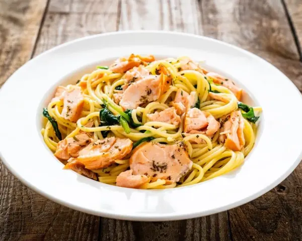 Makaron spaghetti z łososiem i szpinakiem na białym talerzu, na drewnianym tle.