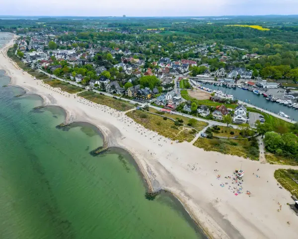 Luftaufnahme eines Strandes mit grüner Ostsee, Häusern und einem Yachthafen. Ein idyllischer Ort für ruhige Orte an der Ostsee.