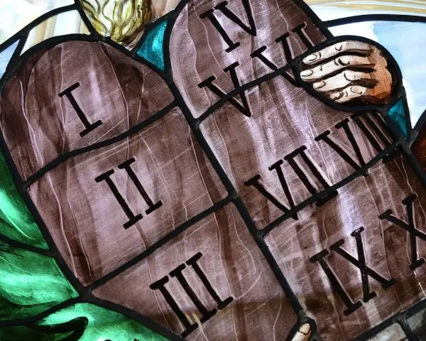 Witraż przedstawia kamienne tablice z wyrytymi cyframi rzymskimi, symbolizujące dekalog przykazania. Widoczne są cyfry I, II, III, IV, V, VI, VII, VIII, IX, X.