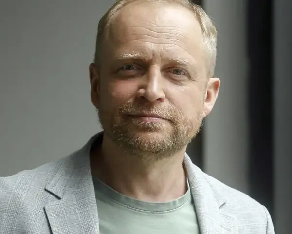 Piotr Adamczyk, znany z wielu filmów, seriali i programów, w jasnej marynarce i zielonej koszulce.