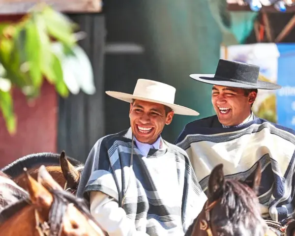 Deux huasos rient joyeusement à cheval, vêtus de ponchos traditionnels et de chapeaux.