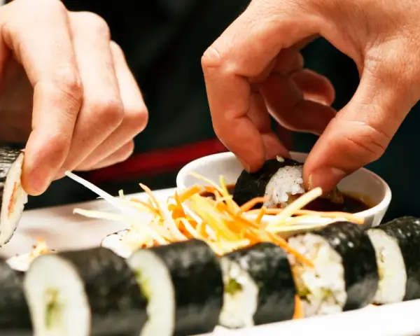 Ręce zanurzają sushi w sosie sojowym. Czy sushi można jeść na drugi dzień? To zależy od świeżości składników i sposobu przechowywania.