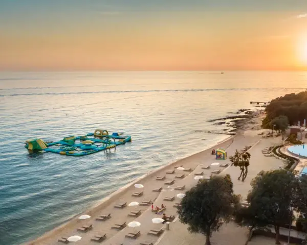 Zachód słońca nad morzem przy plaży z dmuchanym placem zabaw i basenem. Idealne miejsce na wakacje w camping Vrila.