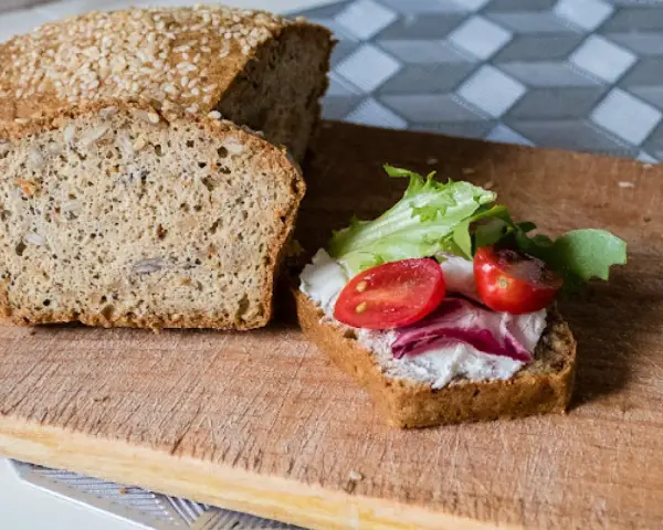 Keto chleb majonezowy przepis: kromka z serkiem, pomidorkami i sałatą obok bochenka z ziarnami.