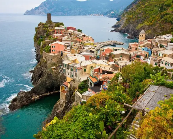 Kolorowe domy Cinque Terre na klifie, idealne na wakacyjne loty do Włoch.
