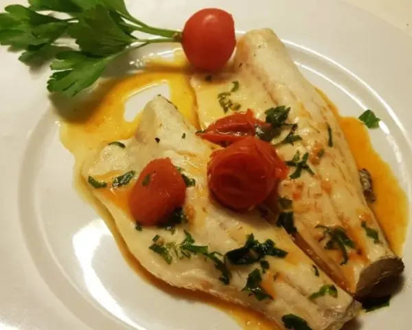 Filetti di branzino in padella con pomodorini e prezzemolo, un piatto leggero e saporito.