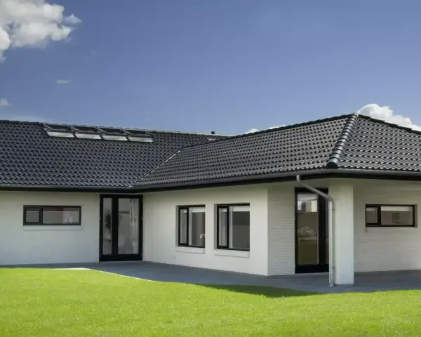 Casa moderna con tetto a padiglione scuro, finestre a tetto e prato verde.
