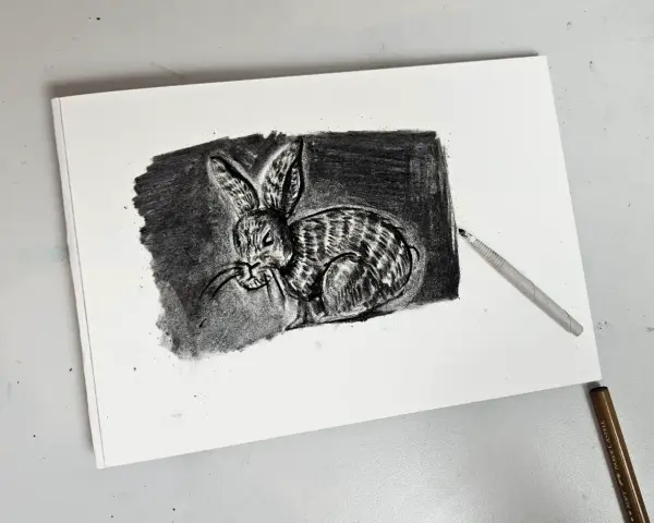 Un detallado dibujo carboncillo de un conejo con rayas, con un lápiz de carboncillo apoyado sobre el papel.