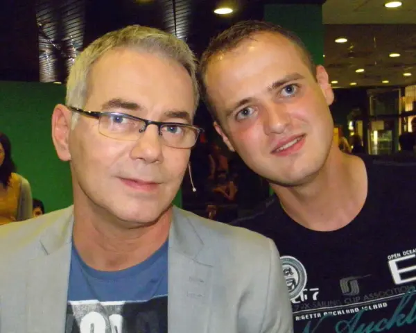 Tomasz Kammel i młody fan pozują do zdjęcia. Tomasz Kammel w szarym garniturze i niebieskiej koszulce, a obok niego młody mężczyzna w czarnej koszulce z napisem "Auckland".