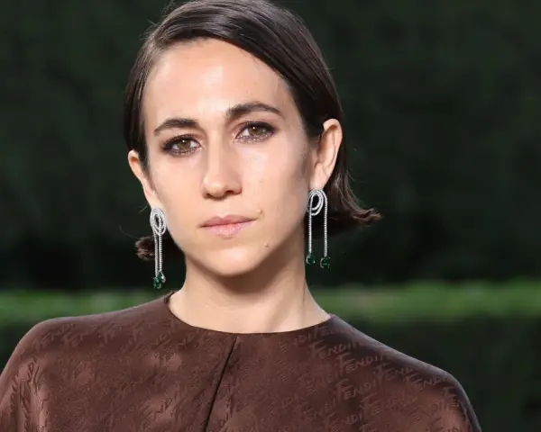 Delfina Delettrez Fendi indossa orecchini pendenti con diamanti e smeraldi, abbinati a un abito marrone con logo Fendi.