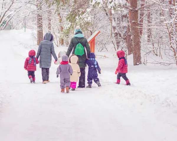Kindergarten-Pflicht: Eine Gruppe Kinder und Erzieherinnen stapfen durch tiefen Schnee im Wald.