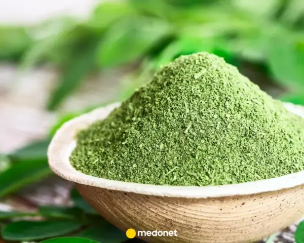 Zielony proszek z liści moringa w miseczce, otoczony świeżymi liśćmi. Odkryj niezwykłe liście moringa właściwości.