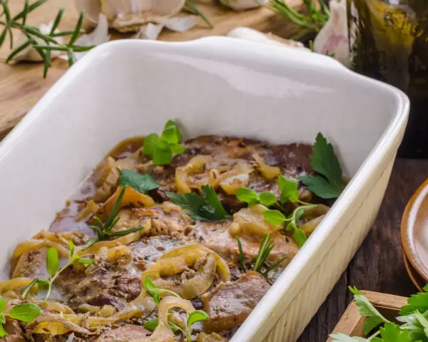 Schab pieczony w piekarniku w naczyniu, duszony z cebulą i ziołami. Aromatyczne danie gotowe do podania.