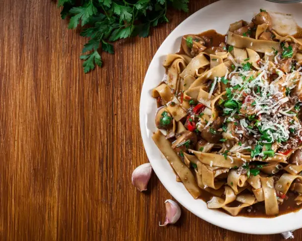 Pyszne danie z makaronem malfadine czy tagliatelle z grzybami i parmezanem, podane na drewnianym blacie.