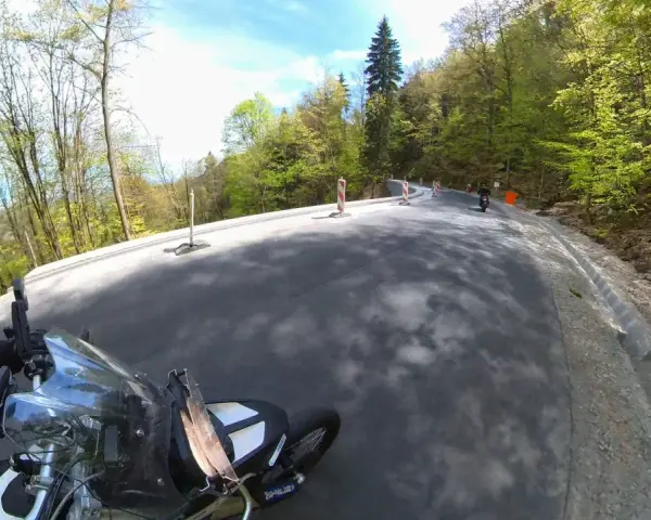 Motocyklista pokonuje krętą drogę stu zakrętów, otoczoną zielonym lasem.