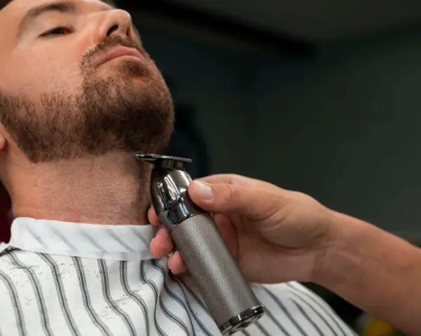 Barbero perfilando la barba ancla de un cliente con una recortadora.
