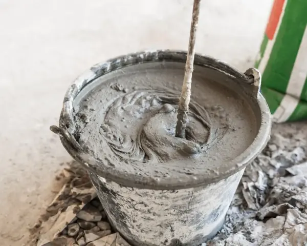 Secchio con malta fresca in preparazione, mostrando la differenza tra malta e cemento. Un sacco di cemento è visibile sullo sfondo.
