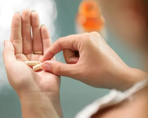 Dłoń trzyma kapsułki, które mogą być lekami do hormonalnej terapii zastępczej.