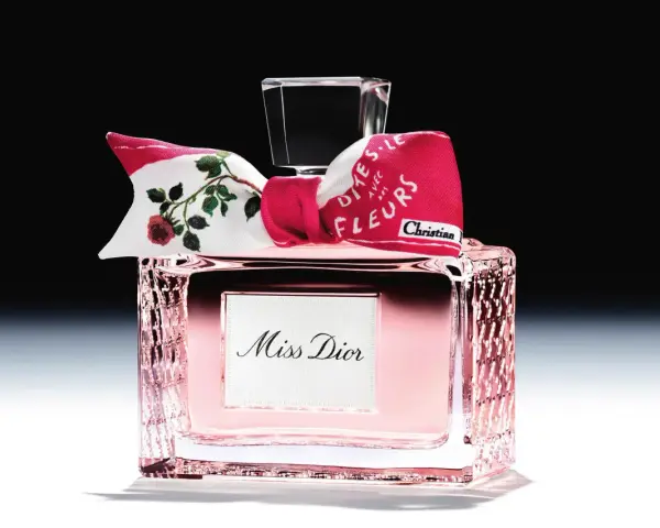 Eleganckie perfumy Miss Dior w różowym flakonie, ozdobione kokardką z motywem róż i napisem "Dites-le avec des fleurs".