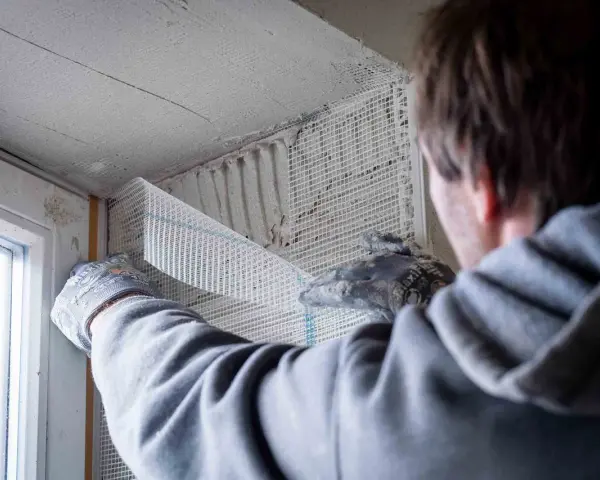 Hand mit Handschuh legt Armierungsgewebe an, um die Fensterlaibung zu verputzen.