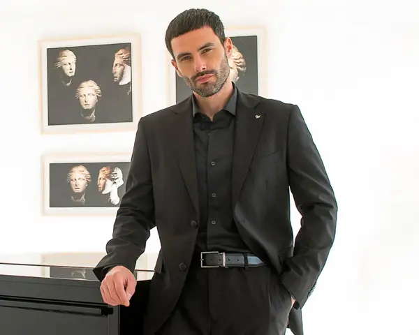Uomo elegante in completo nero, camicia nera uomo abbinamento perfetto. Sfondo con quadri di busti classici.