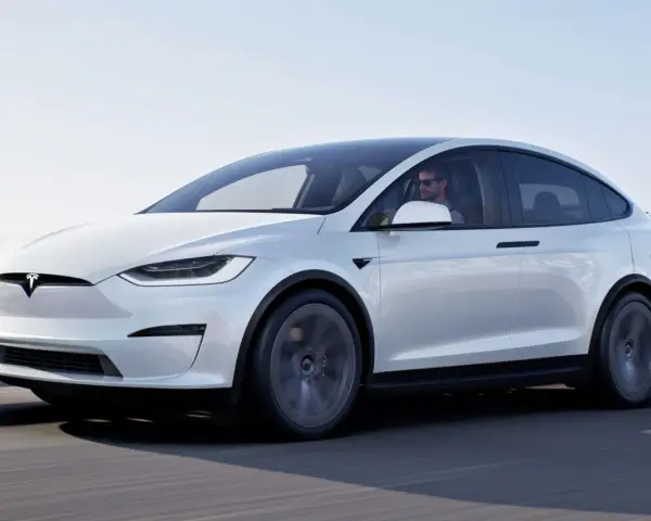 Biały Tesla X w ruchu, kierowca w okularach. Zastanawiasz się nad jego ceną?