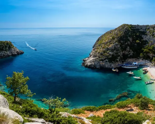 Malownicza zatoka z krystalicznie czystą wodą, plażą i łodziami. Idealne miejsce na wczasy samolotem all inclusive w Albanii.