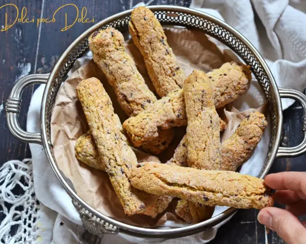 Biscotti senza farina dorati e croccanti, cosparsi di zucchero, in un cestino d'argento. Una mano ne prende uno.