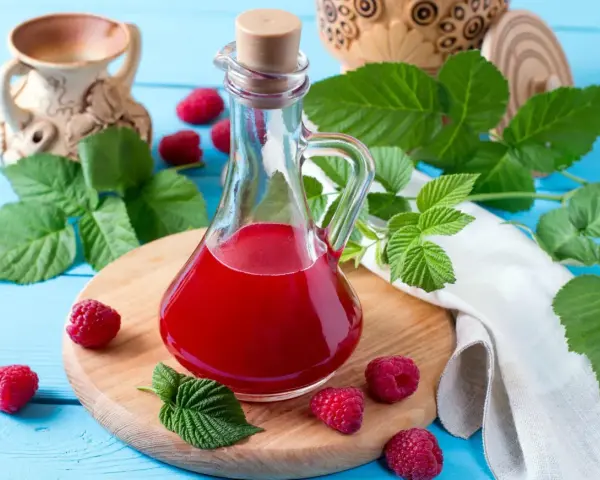 Malinowy ocet balsamiczny do sałatek, deserów, marynat. W butelce z korkiem, otoczony świeżymi malinami i liśćmi.