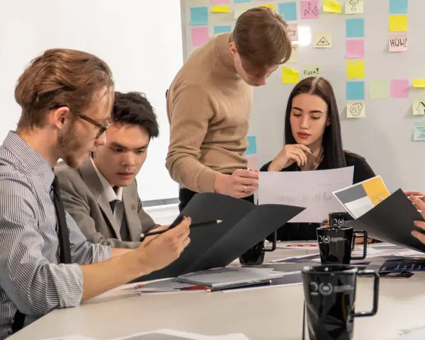 Studenci analizują wykresy, przygotowując się do zajęć z handlu międzynarodowego. Na tablicy notatki i pomysły.
