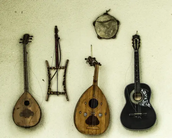 Verschiedene Saiteninstrumente und ein Tamburin hängen an der Wand. Seit wann gibt es Gitarren? Die Geschichte der Gitarre reicht weit zurück.
