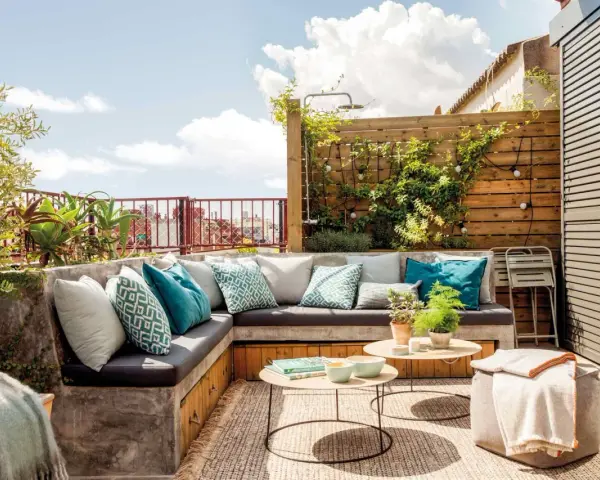 Cómodo rincón de terraza con sofás de obra, cojines turquesas y plantas. Ideas para jardineras exteriores que inspiran relax.