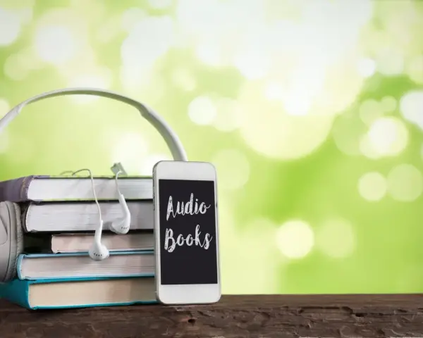 Słuchawki, stos książek i telefon z napisem "Audio Books" – idealne połączenie do odkrywania najpiękniejszych słuchowisk dla dzieci.