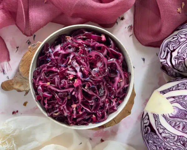 Insalata di cavolo cappuccio rosso, condita con petali di fiori, accanto a un cavolo cappuccio rosso tagliato a metà.