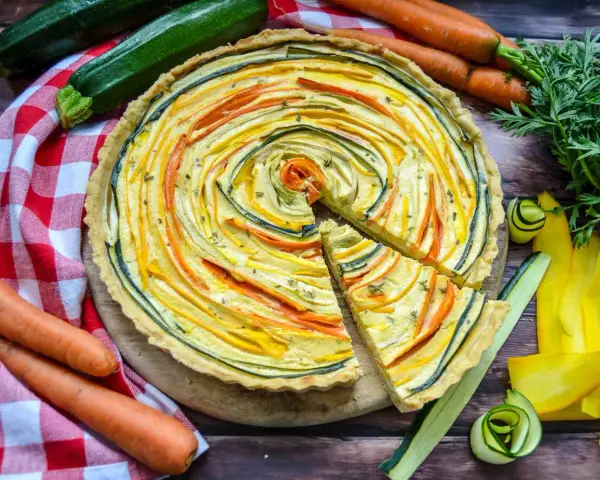 Eine bunte, vegetarische Quiche mit Zucchini und Karotten, kunstvoll im Kreis arrangiert. Frisch und lecker!