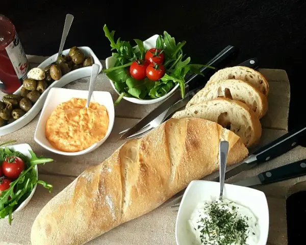 Eine köstliche italienische Brotzeit mit Baguette, Oliven, Tomaten, Rucola und Dips.