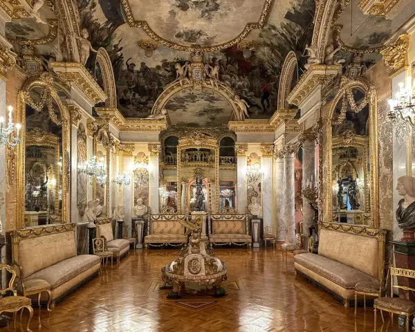 Złocone wnętrze pałacowe, przypominające muzeum w Madrycie, z malowidłami na suficie i bogatymi zdobieniami.