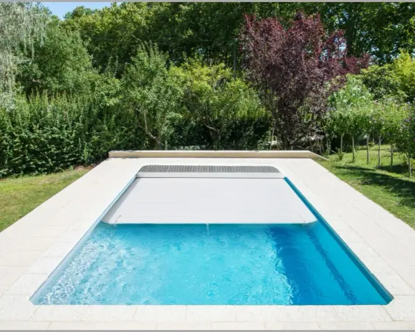 Piscina con cubierta automática, lista para reformar y disfrutar del verano. Rodeada de vegetación exuberante.