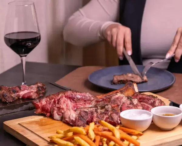 Idealne wino do dziczyzny? Czerwone, pełne, jak to w kieliszku obok soczystego steka i frytek. Ktoś kroi kolejny kawałek.