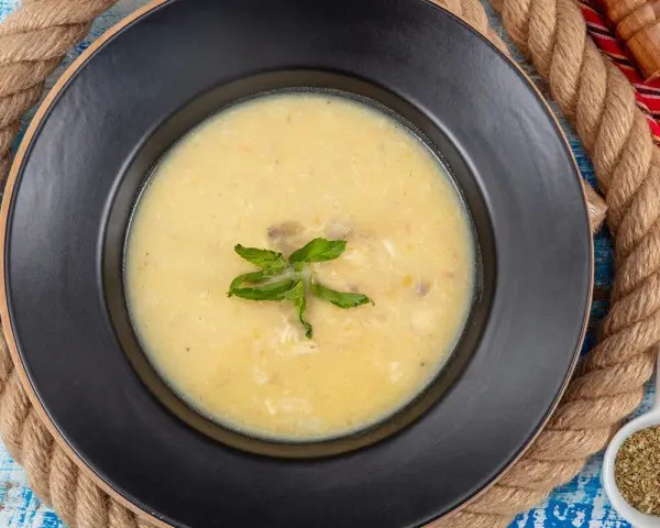 Un plato de sopa de pescado cremoso y caliente, decorado con hojas verdes, sobre un fondo rústico.